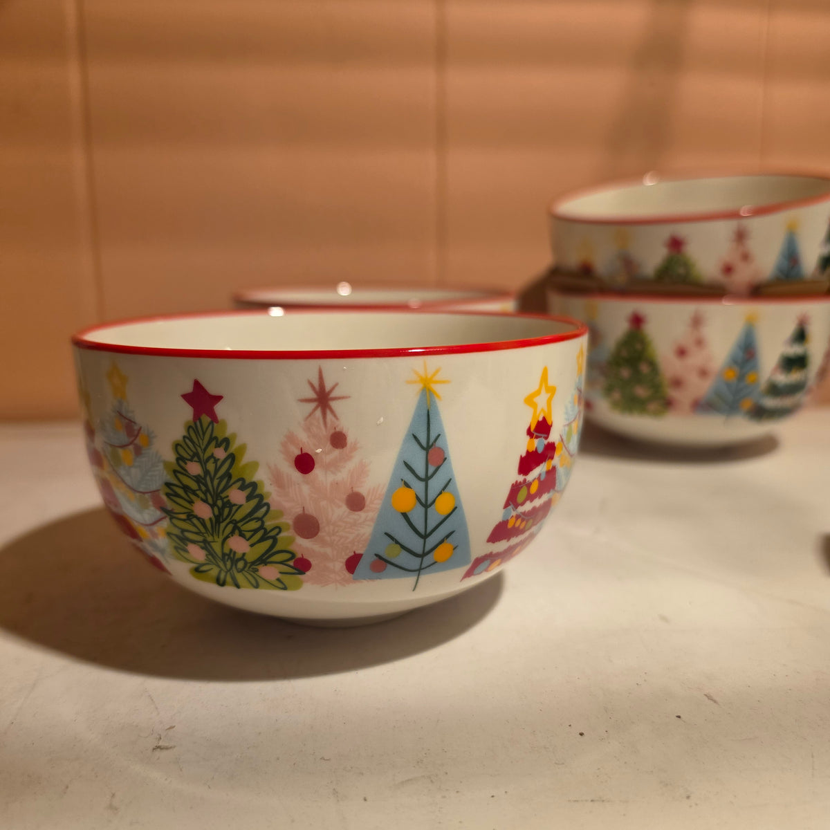 A set of white ceramic bowls decorated with colorful Christmas tree illustrations.
